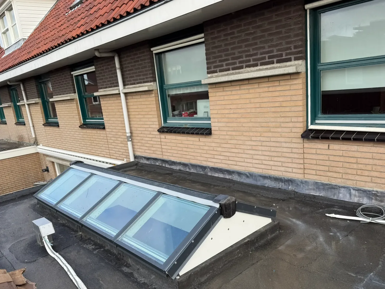 De lichtstraat op het platte dak van de aanbouw, tegen de gevel van de woning.