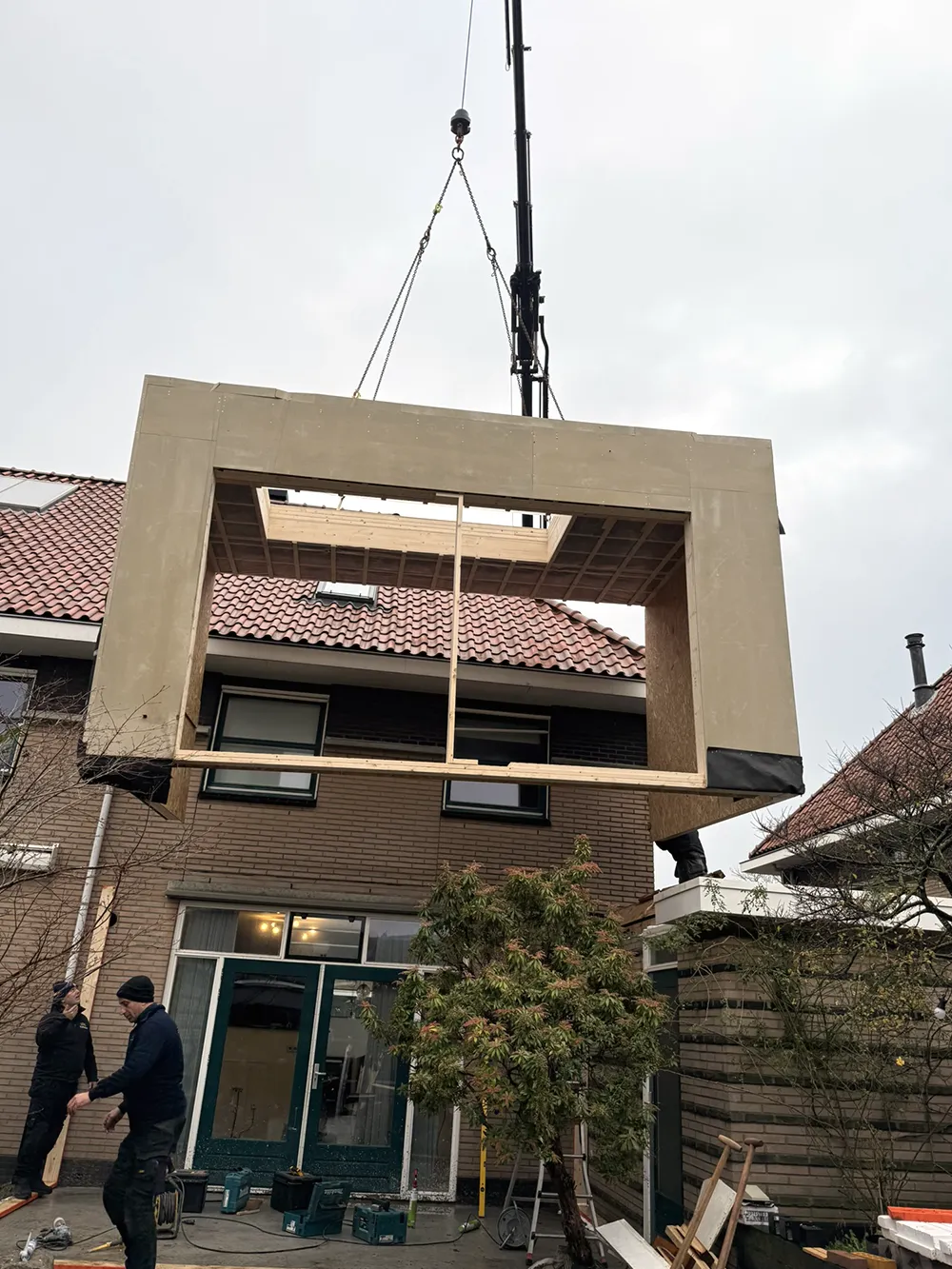 Een groot gevelelement hangt aan de kraan boven de woning.