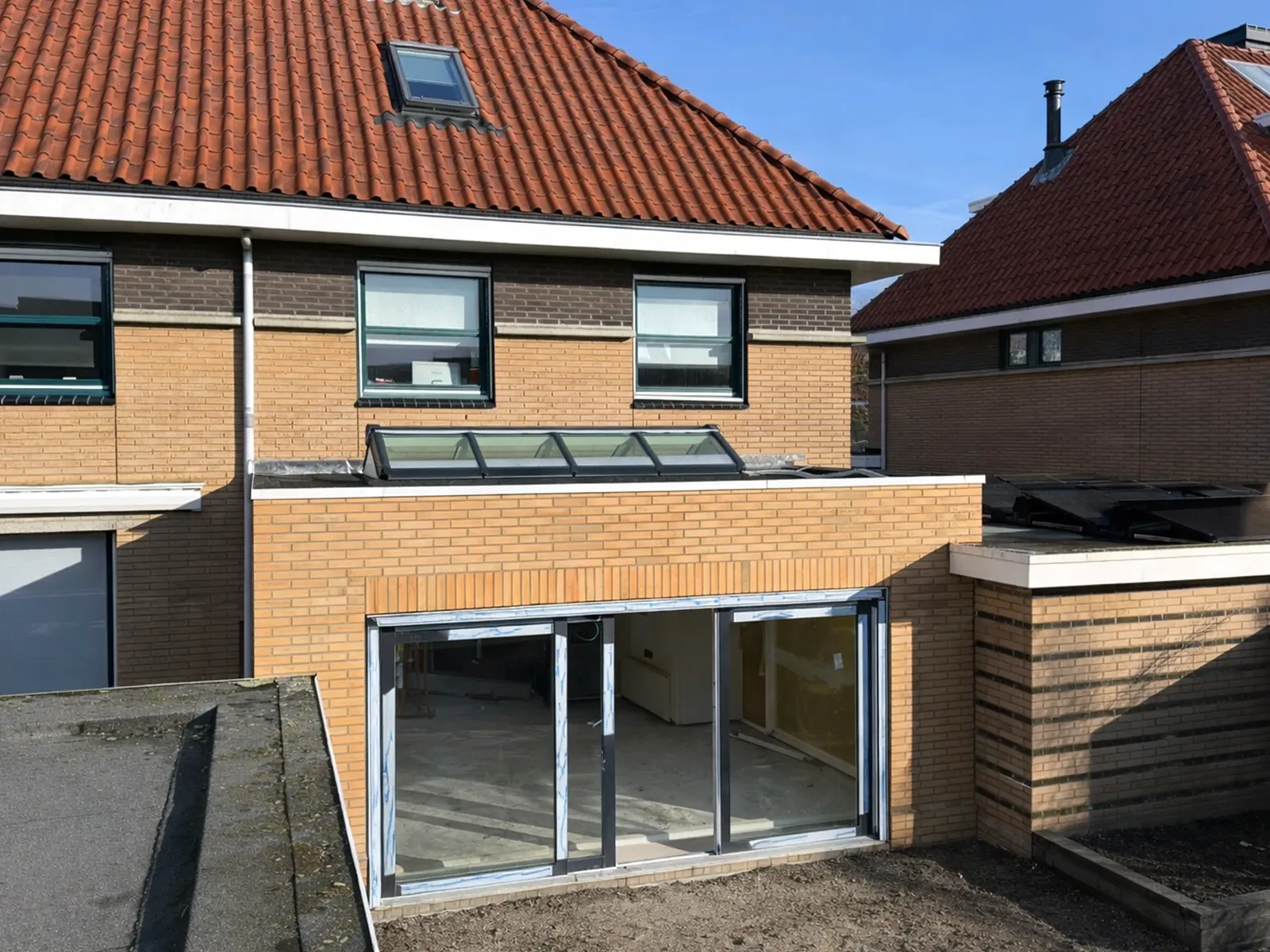 De aanbouw van buiten, met gemetselde gevel, plat dak en de lichtstraat tegen de woning aan.