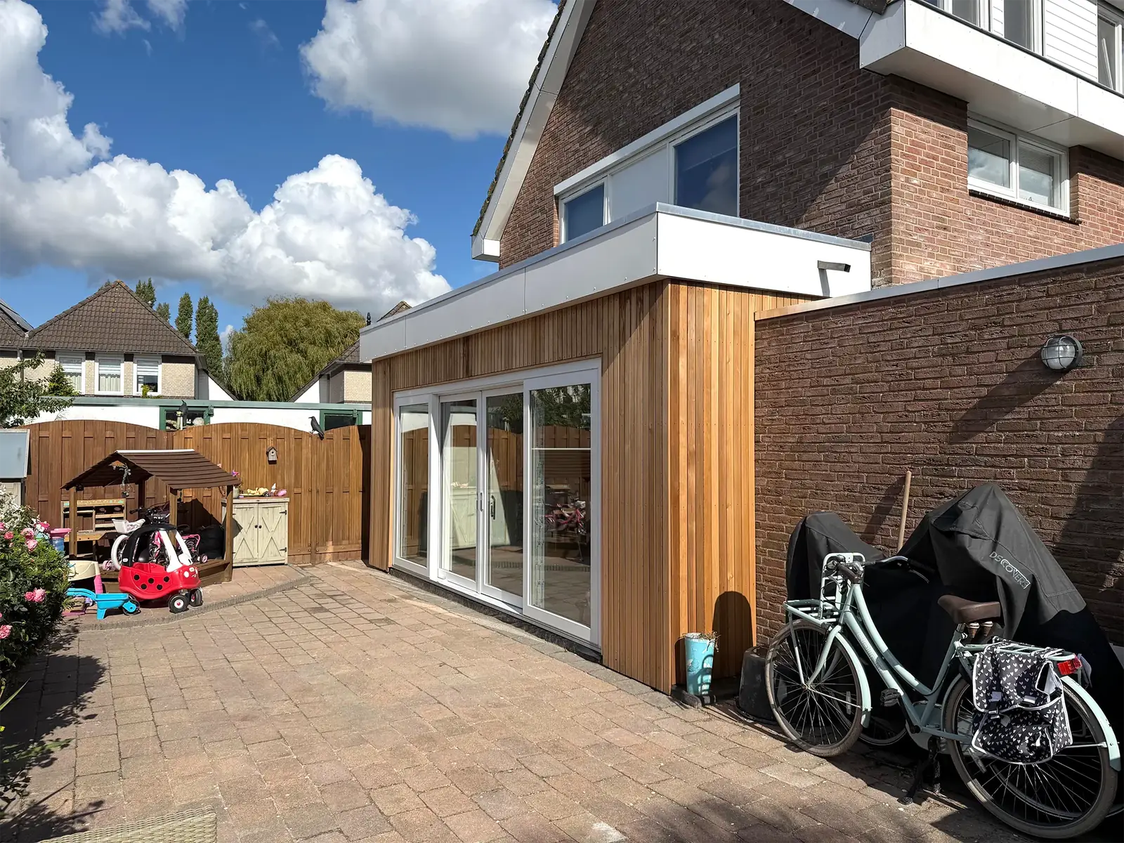 De aanbouw vanaf het terras gezien, met de houten gevel tegen de bestaande muur.