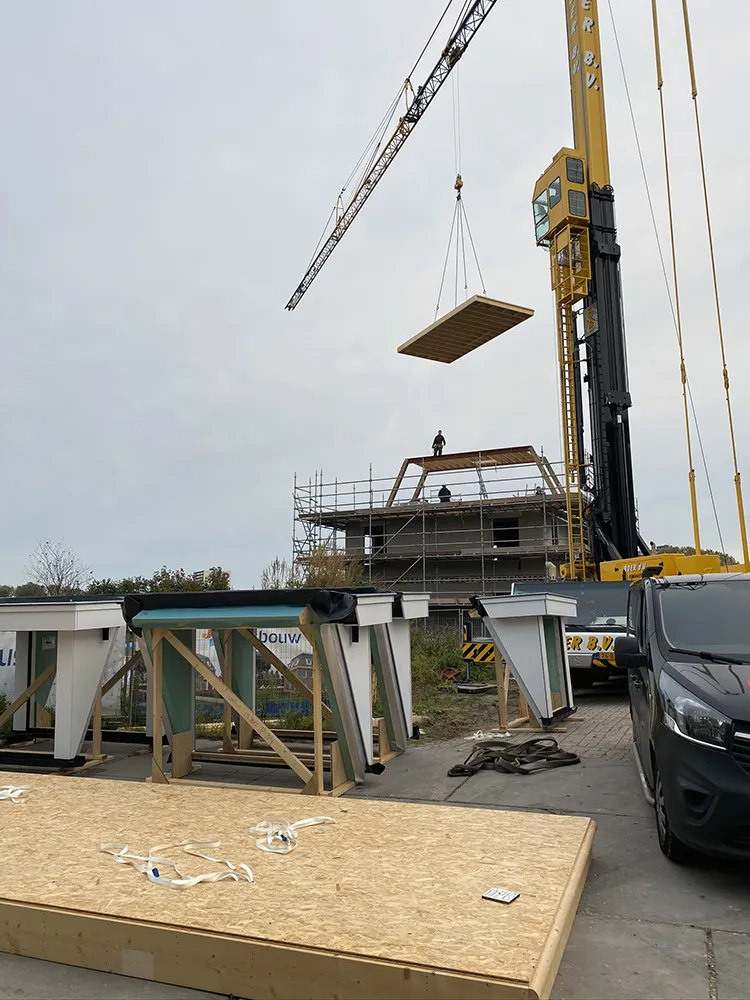 Een vloerelement hangt aan de torenkraan boven de bouwplaats.